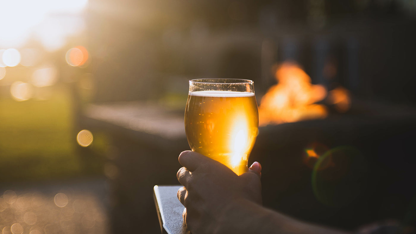 Craft beer enthusiast sitting in an Adirondack chair in front of a fire holding a fresh NY craft beer.